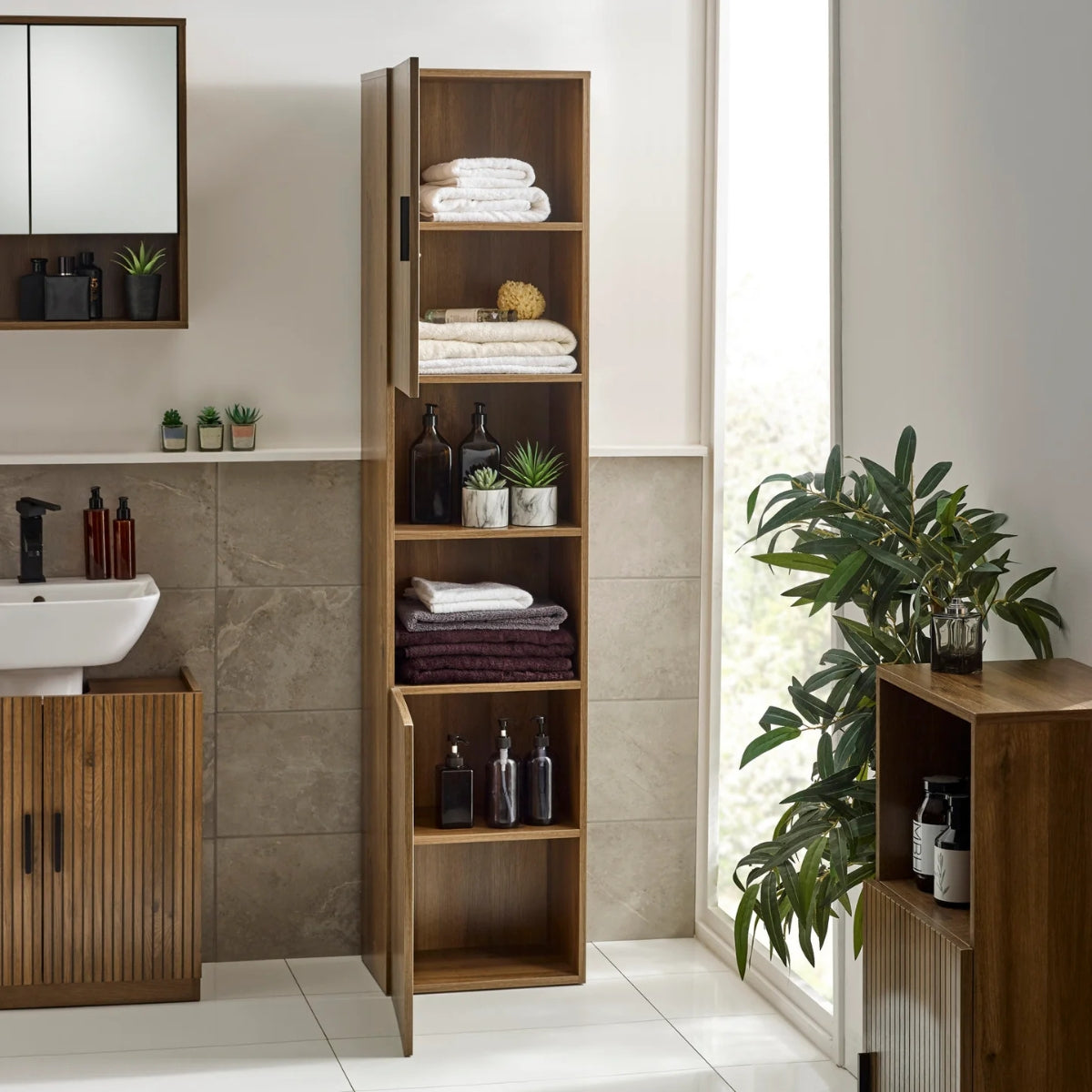 Hampshire tall wooden cabinet in a bathroom with shelves filled with towels and bottles, next to a sink and mirror.