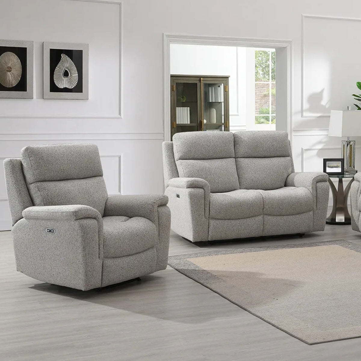 Hector grey upholstered recliner chair and matching loveseat in a bright, modern living room with white walls, a beige rug, and light wood flooring.