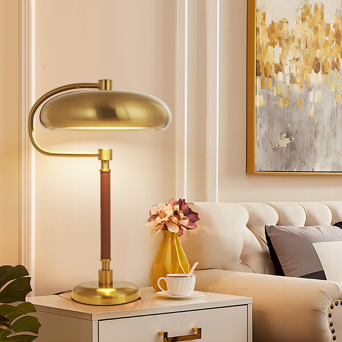 Gold table lamp on a side table with a cup and flowers in a living room setting.