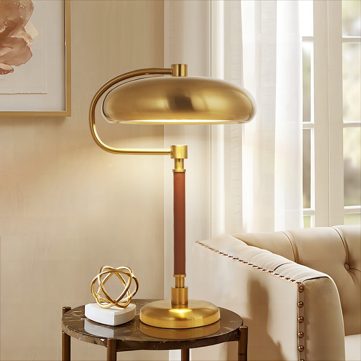 Gold table lamp on a side table with a beige sofa and framed artwork in the background
