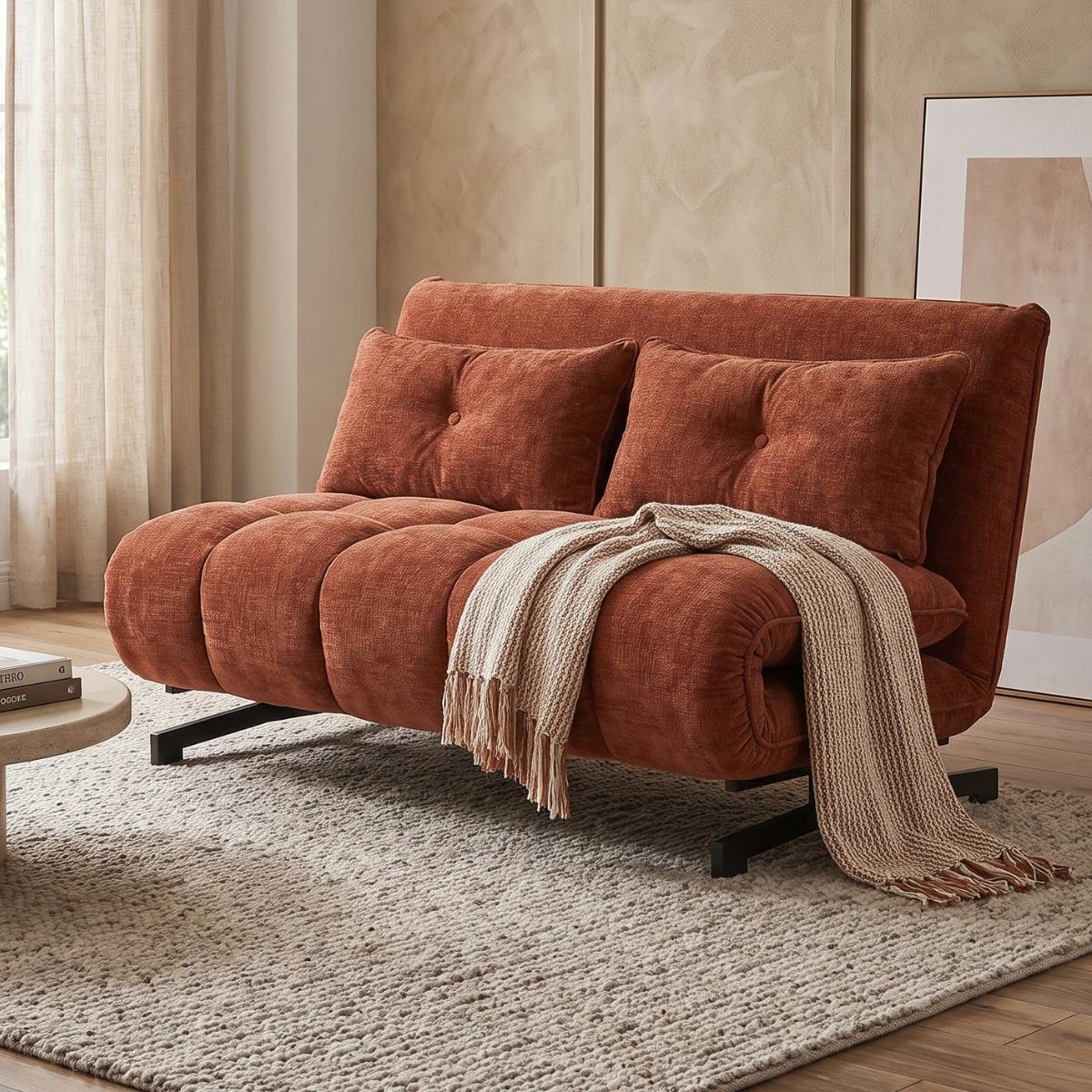 An orange-brown velvet convertible sofa bed with two matching pillows and a beige throw blanket, styled in a warm, modern living room setting.