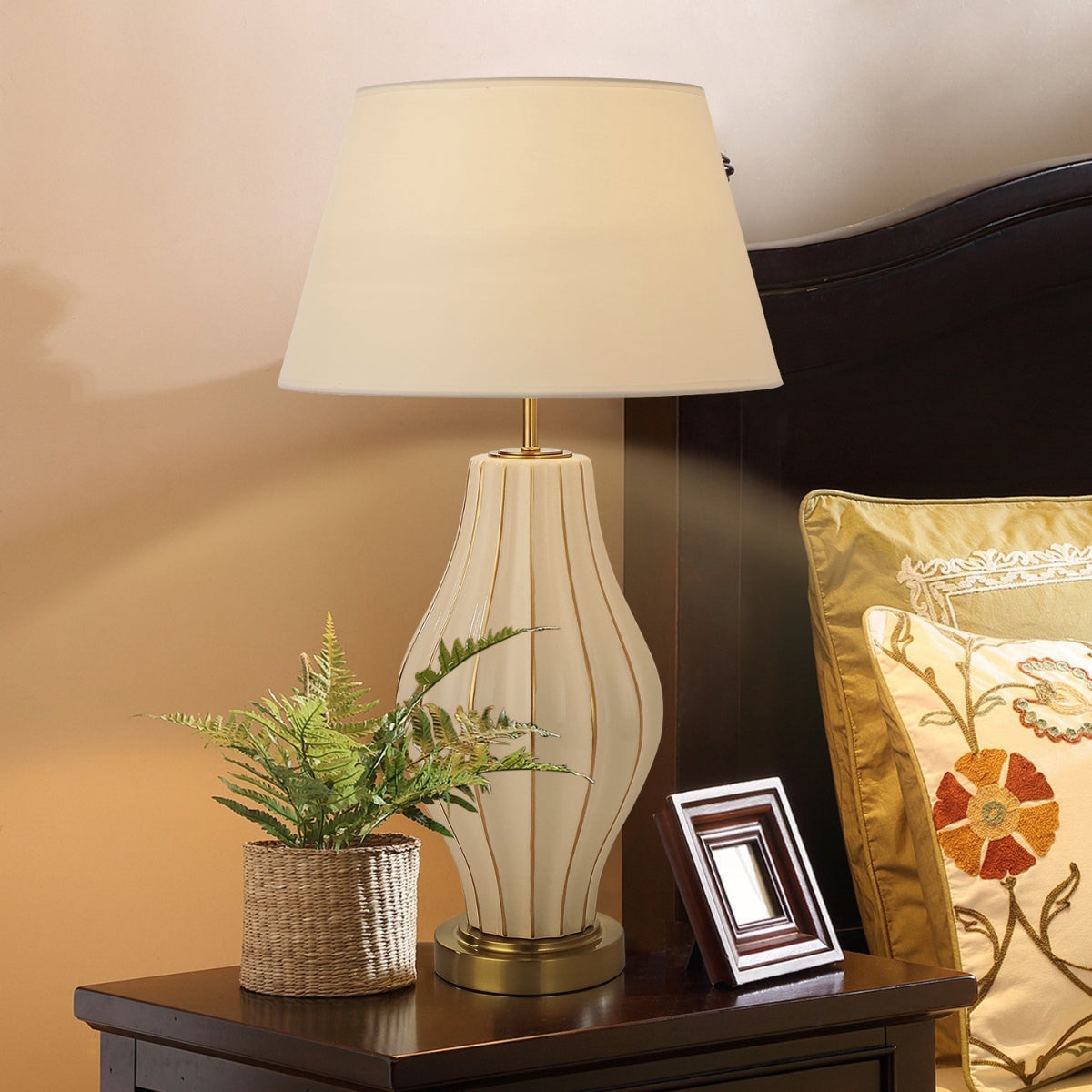 Decorative lamp on a nightstand with a plant and photo frame.