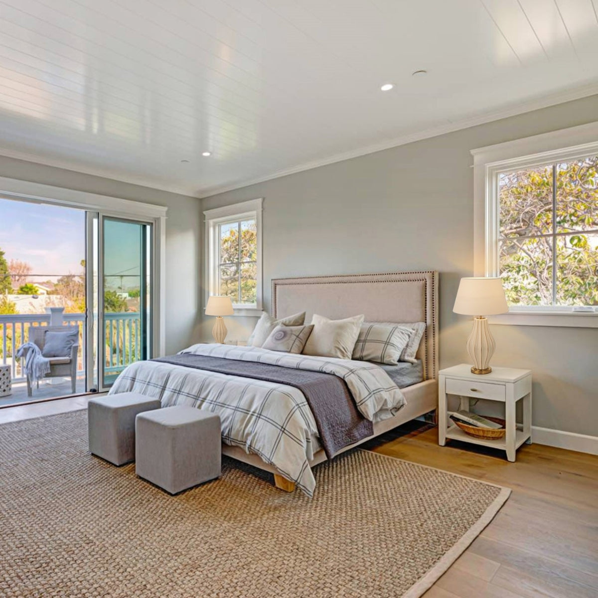 Modern bedroom with a bed, side table, and chairs near a window.