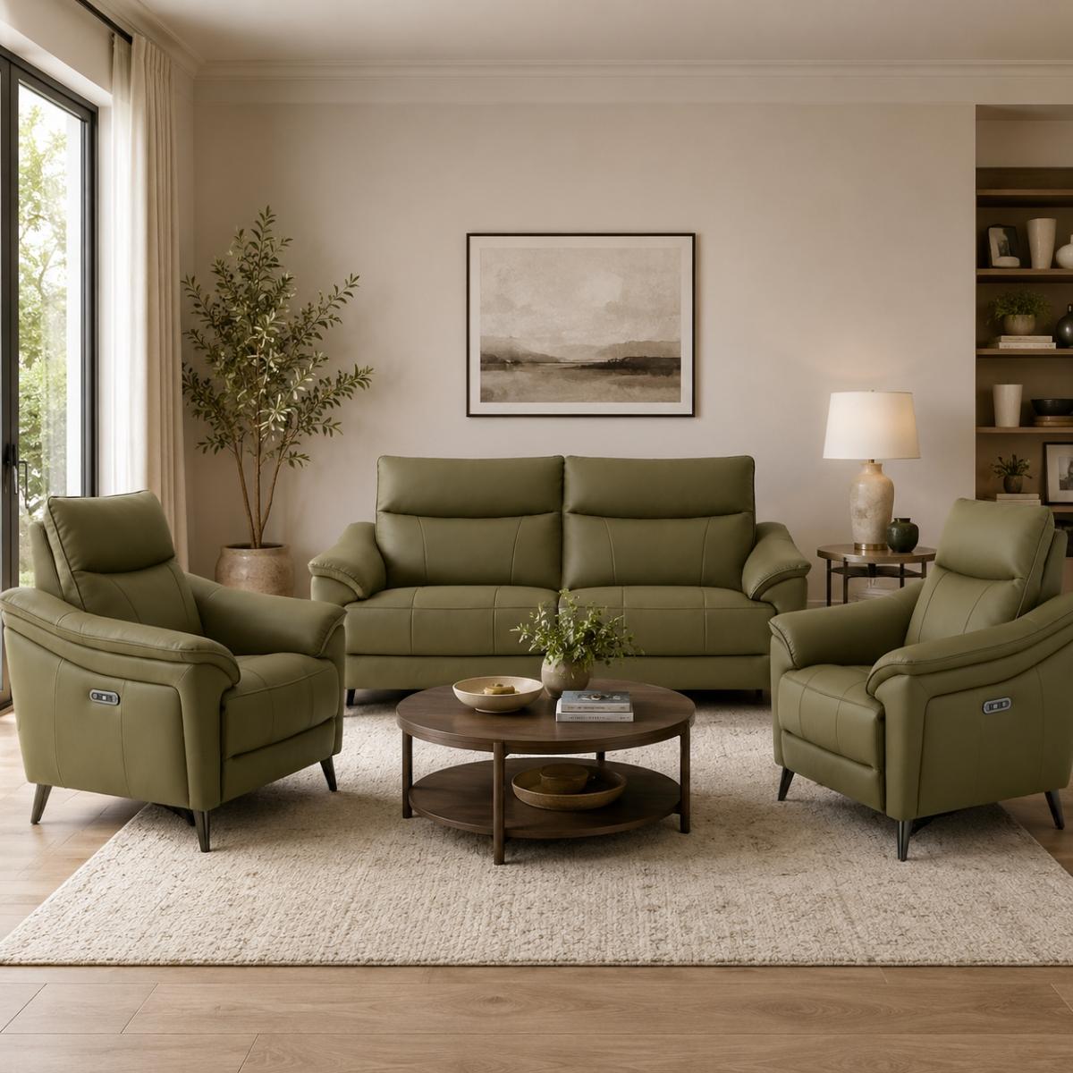A staged living room featuring the Hamish green sofa, two matching armchairs, a round wooden coffee table, and a textured cream rug on a light wood floor. The room has beige walls, a window with curtains, a potted plant, and a built-in bookshelf.
