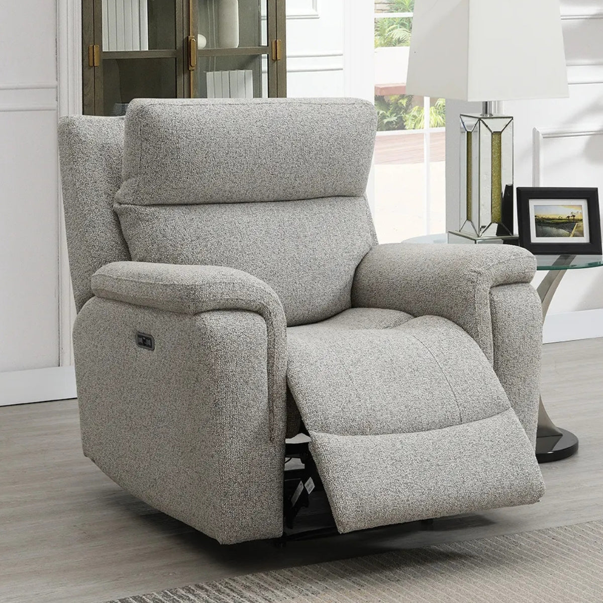 Hector grey textured recliner chair with the footrest extended, shown in a modern living room setting next to a glass-top side table with a lamp.