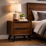 Wooden nightstand with lamp and books next to a bed in a bedroom setting