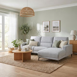 Johnson grey fabric sectional sofa with a chaise lounge in a bright, modern living room. The sofa is styled with neutral-toned throw pillows and a beige throw blanket, set on a large woven jute rug.