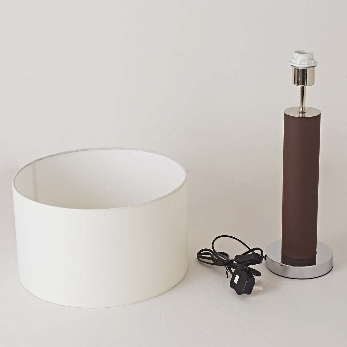 Lamp components including a white shade, brown cylindrical base, and black power cord on a light grey background.