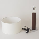 Lamp components including a white shade, brown cylindrical base, and black power cord on a light grey background.