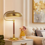 Gold table lamp on a side table with a cup and flowers in a living room setting.