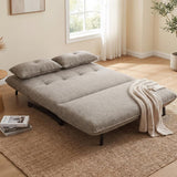 A gray fabric futon sofa bed with two matching pillows and a draped cream throw blanket, shown in a bright, modern room with a window, curtains, and a woven rug.