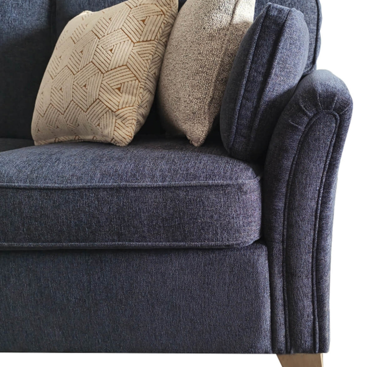 Close-up of a dark blue upholstered sofa with two decorative throw pillows, one in textured beige fabric with a geometric pattern and one in a solid taupe fabric, set against a plain white background.