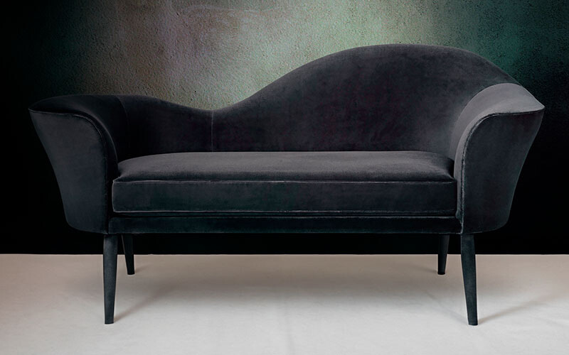 Black velvet chaise lounge with curved edges and black wooden legs.