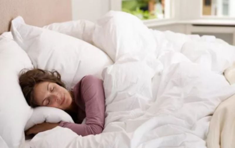 Woman sleeping on bed with white sheets.