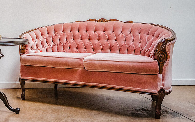Curved pink velvet loveseat with button features and wooden legs.