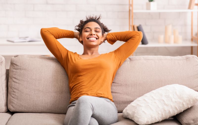 Smiling girl sitting on grey linen sofa with cream cushion.