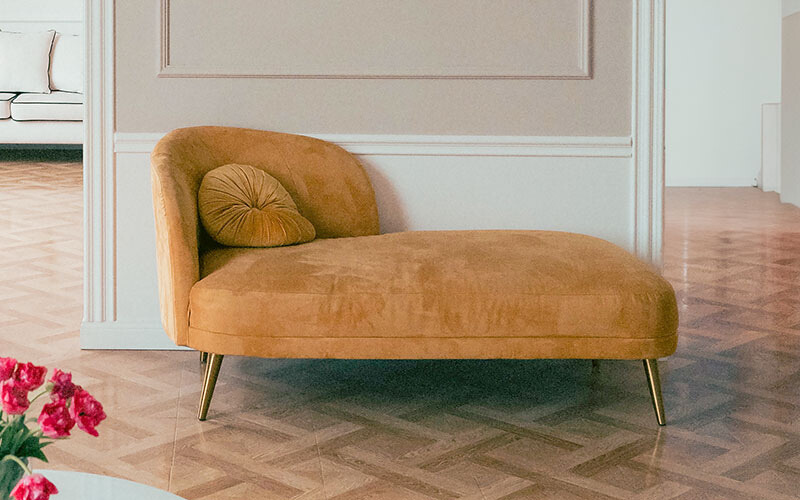 Mustard velvet chaise lounge with cushion and gold legs.