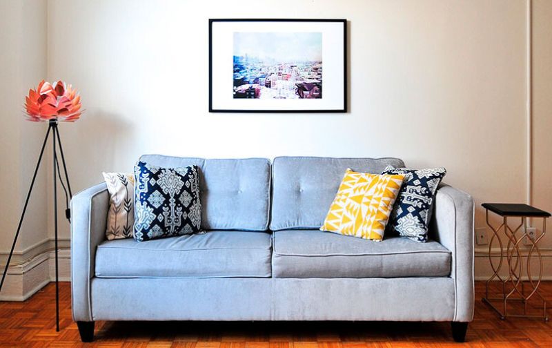 Light blue two seater sofa with cushions and orange feature lamp.