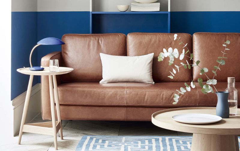 Brown leather sofa with white cushion against a blue wall.
