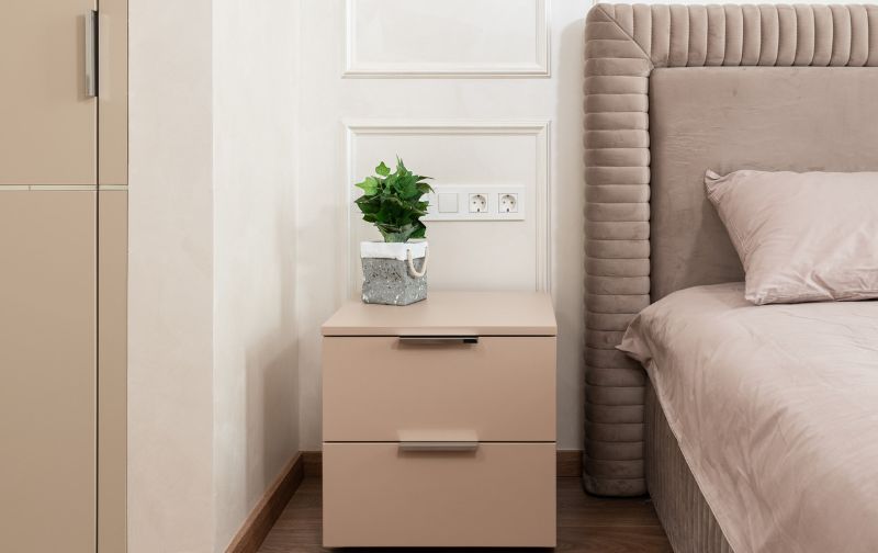 Taupe bedside locker with green plant.