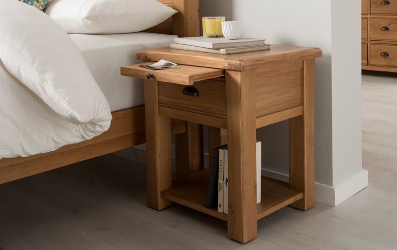 Wooden bedside locker with open sliding drawer, candle and books.