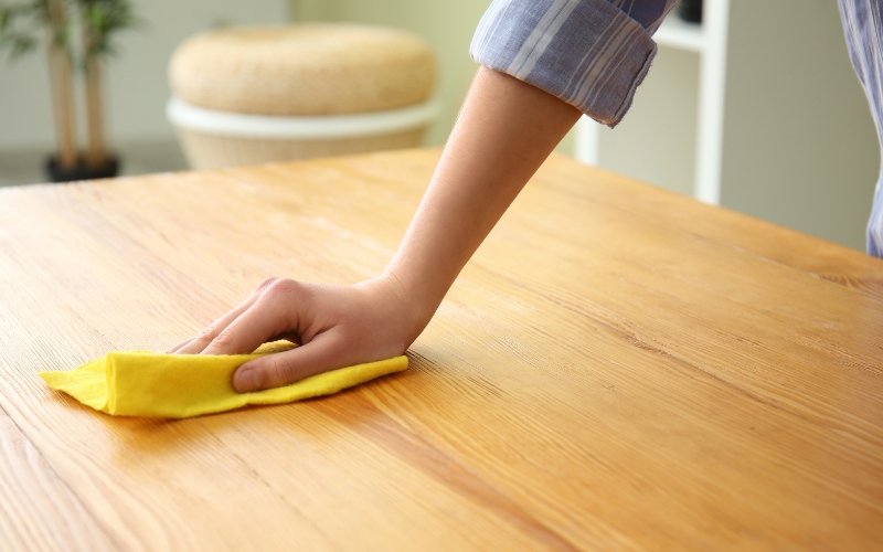 a hand with a yellow cloth cleaning a wooden table