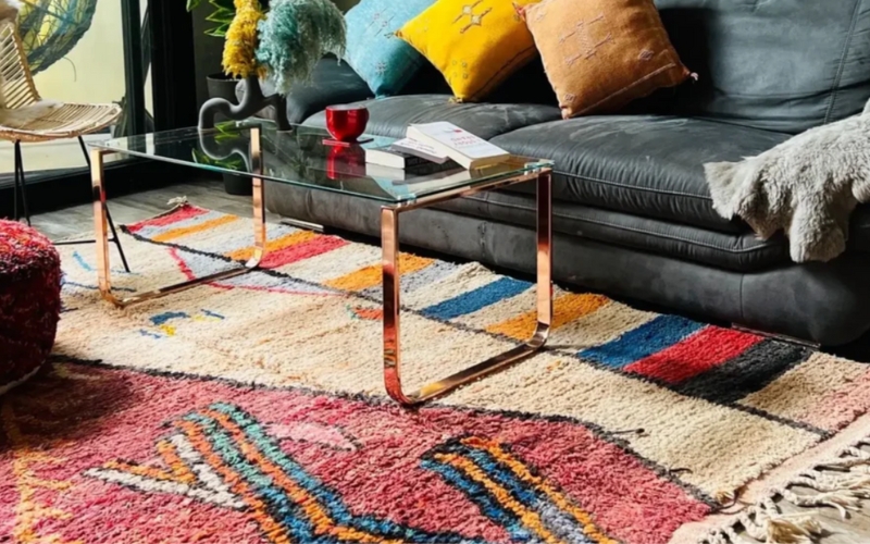 a couch on a moroccan rug with a glass table and colorful pillows