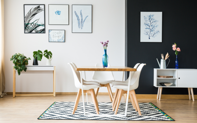 a dining table with white plastic chairs in a room with art on the wall