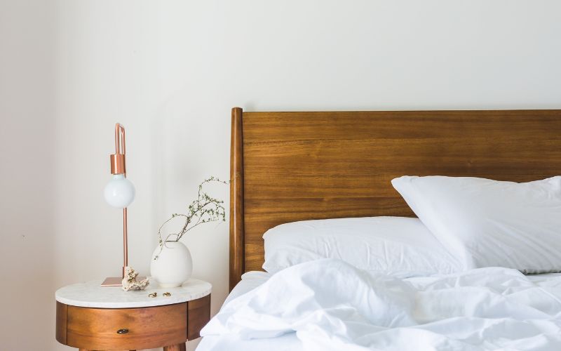 a bed with a white bedding and a white vase on a table